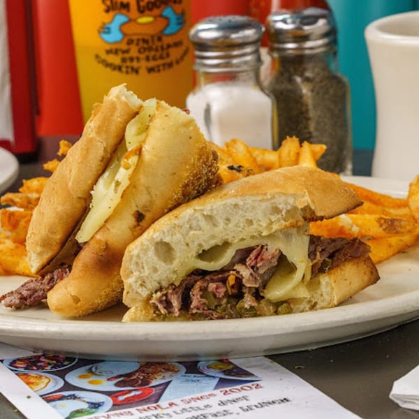 A Slim Goodies Diner cheesesteak sandwich with fries, salt and pepper shakers, and a drink.
