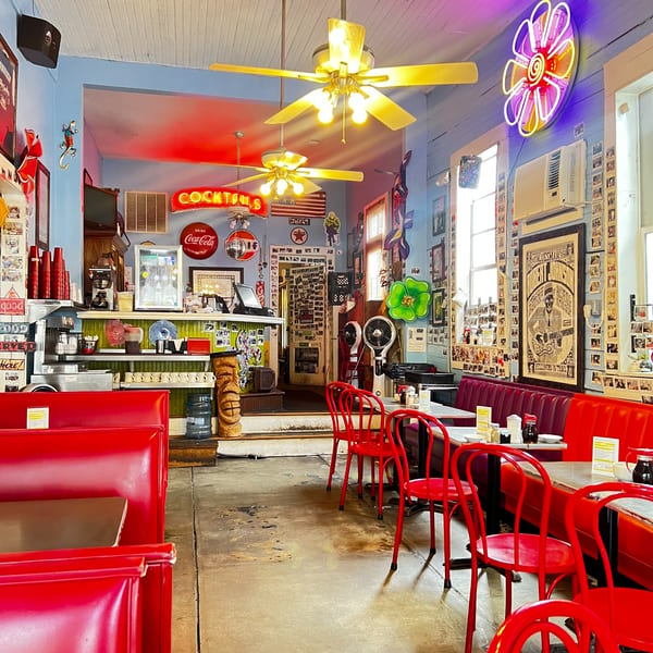 Slim Goodies Diner interior with red booths, chairs, and neon signs, including a "COCKTAILS" sign.