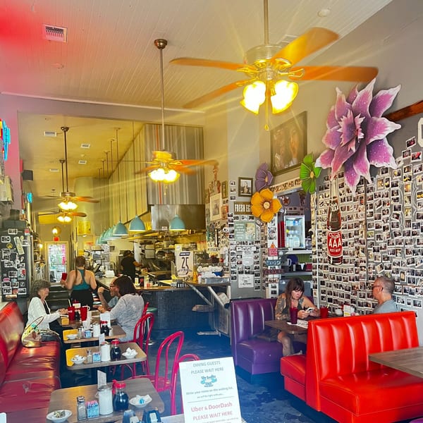 Interior of Slim Goodies Diner with patrons seated at red and purple booths, and a busy kitchen.