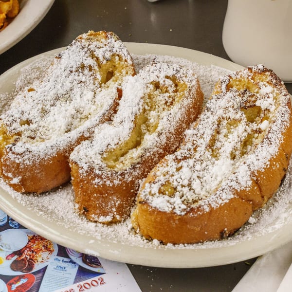 Three slices of golden-brown French toast, generously dusted with powdered sugar, on a white plate.