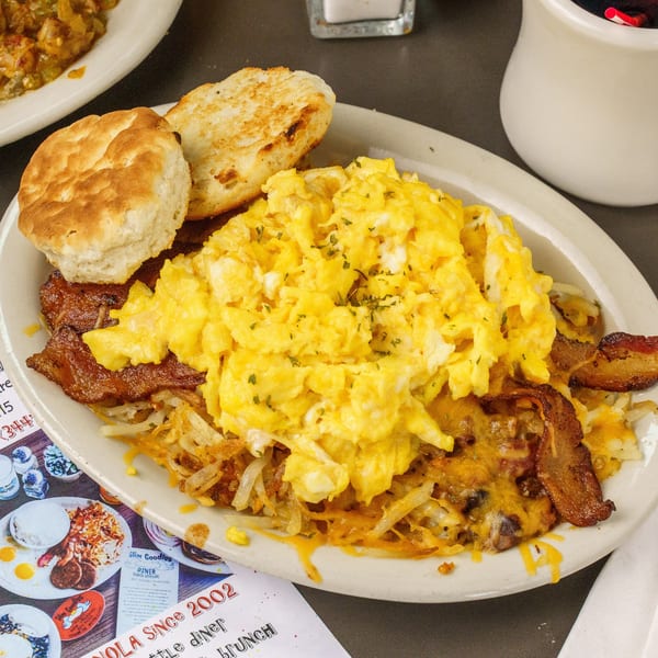 A plate of scrambled eggs, hash browns with cheese, bacon, and two biscuits from Slim Goodies Diner.
