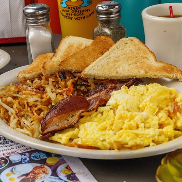 A diner breakfast plate with scrambled eggs, crispy hash browns, bacon, and toast.