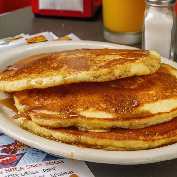 Stack of golden pancakes with syrup on a white plate at Slim Goodies Diner.