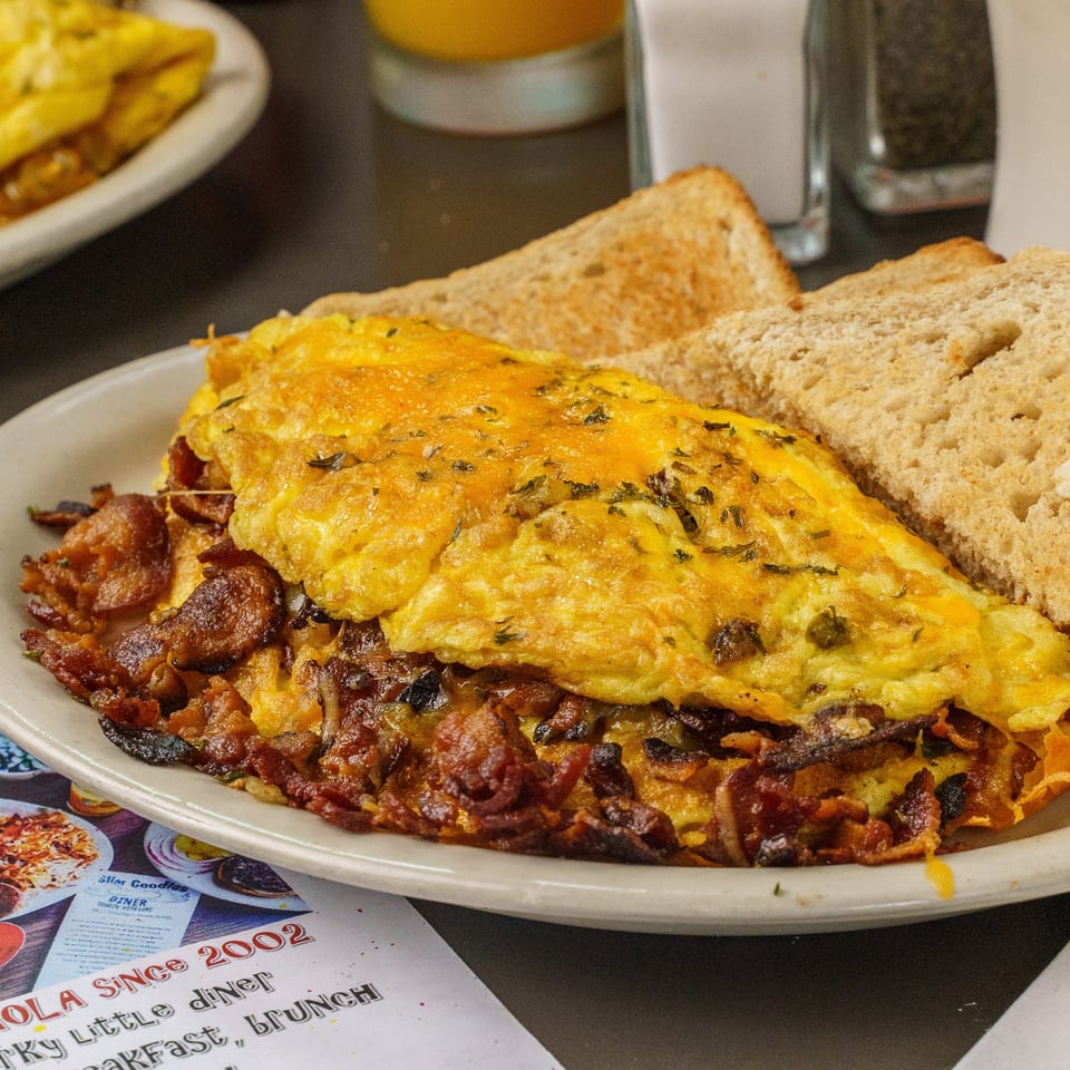 A Slim Goodies Diner omelet with cheese and herbs, bacon, and toast on a white plate.