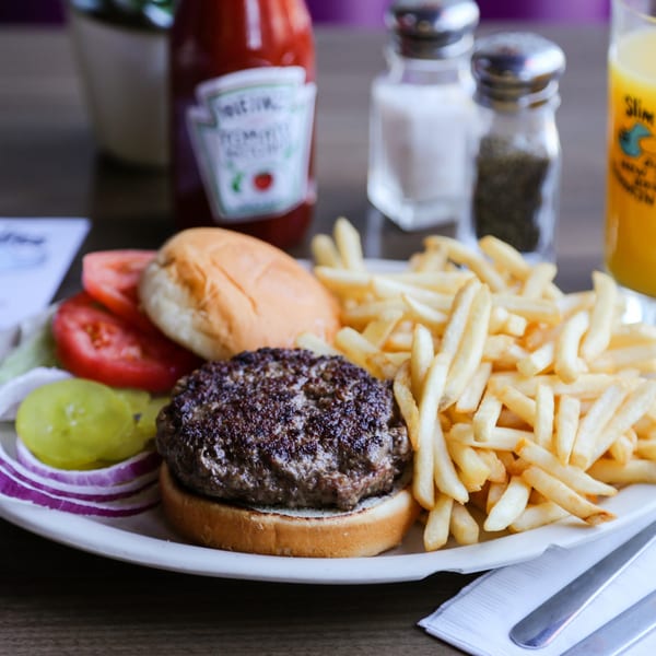A Slim Goodies Diner burger with fries, pickles, onions, tomatoes, and ketchup on a white plate.