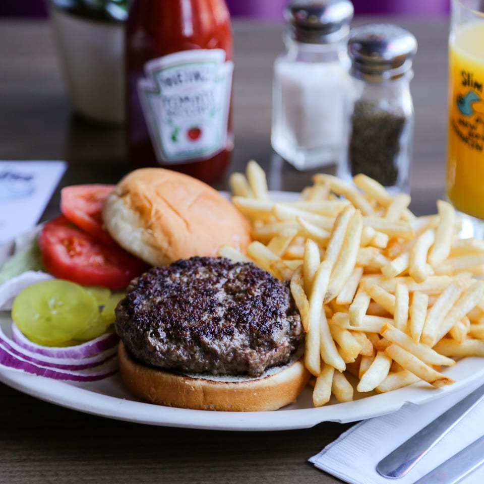 A Slim Goodies Diner burger with fries, pickles, onions, tomatoes, and ketchup on a white plate.